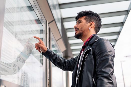 young latin man consulting the public transportation map at the bus stop, concept of sustainable transportation and urban lifestyle