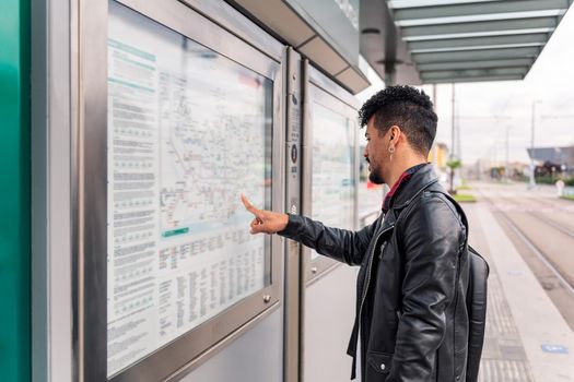 modern young man consulting the public transportation map at the tramway stop, concept of sustainable transportation and urban lifestyle