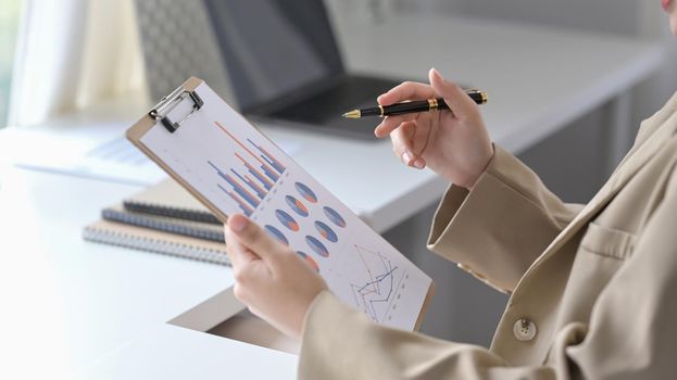 Cropped shot businesswoman sitting at comfortable workplace and analyzing financial graph.