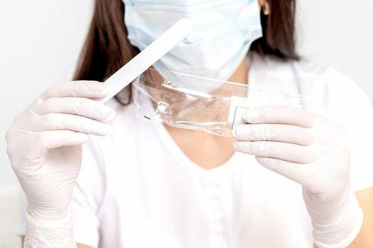 Portrait of a manicure master in a white coat and white mask on her face with nail files in her hand.