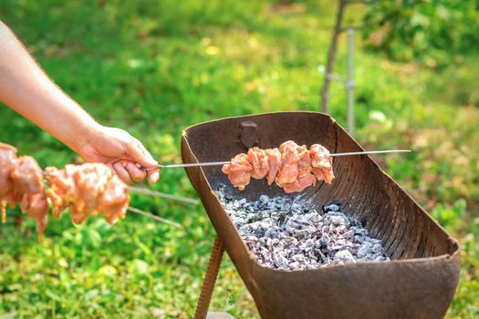 Hands of man prepares barbecue meat on skewer by grill on fire outdoors