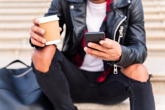 detail of the hands of an unrecognizable stylish young man consulting the phone with a coffee in his hand, concept of technology and urban lifestyle