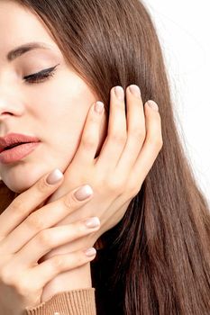 Portrait of pretty young woman touching face with her hand beige manicure on white background with copy space.