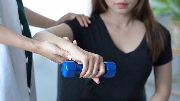 Physiotherapist giving exercise with dumbbell treatment about arm and shoulder of female patient. Physical therapy concept