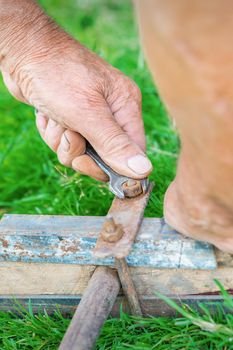 hand of an elderly man twisting the nut with a wrench outdoors. Repair by wrench.