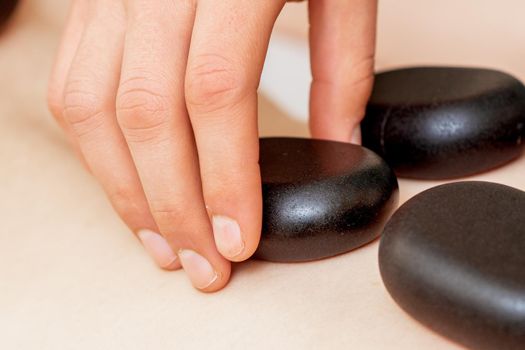 Back massage on back of woman with black hot stones close up.