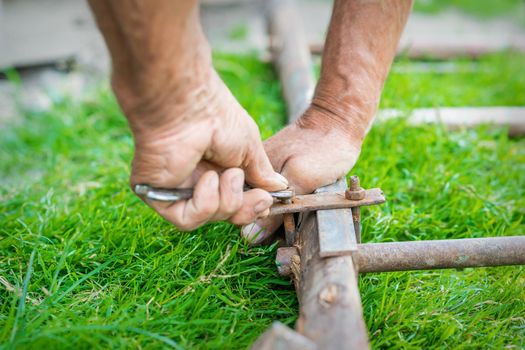 hand of an elderly man twisting the nut with a wrench outdoors. Repair by wrench.