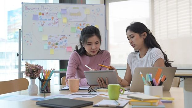 Two focused creative woman designers are working on design project together.