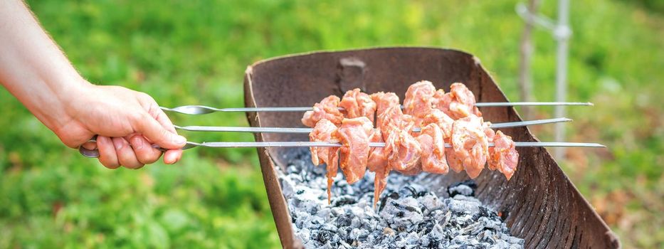 Hands of man prepares barbecue meat on skewer by grill on fire outdoors