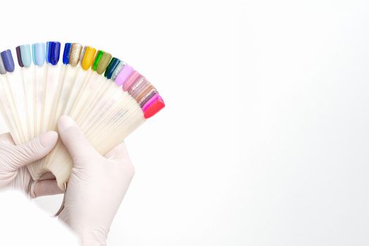 Manicurist hands are holding manicure nail color samples palette on white background.
