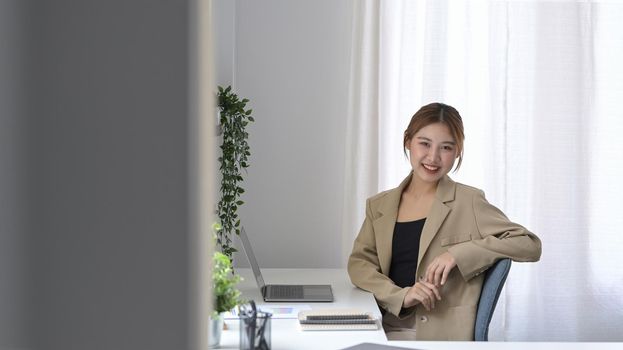 Gorgeous young businesswoman sitting in comfortable workplace and smiling to camera.