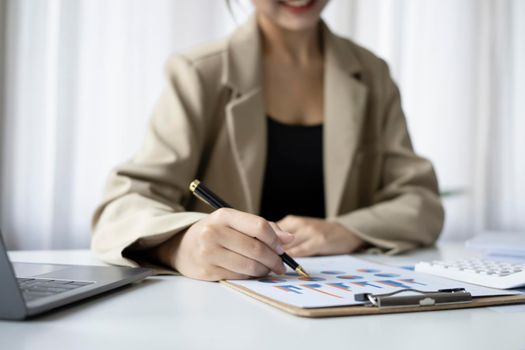 Cropped shot businesswoman holding pen and checking financial reports on white office desk.