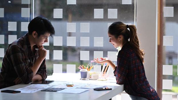 Two designers sitting in bright modern office and discussing about application development for mobile phone.