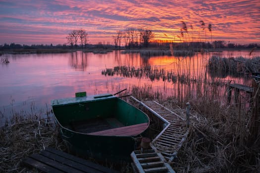 A moored boat at the lake shore and a beautiful colourful sunset, Stankow, Lubelskie, Poland.