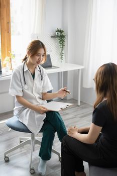 Female doctor in white medical coat giving consultation with patient in clinic or hospital.