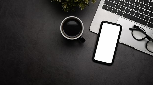 Mockup mobile phone with white screen, laptop computer, coffee cup and eyeglasses on black table.