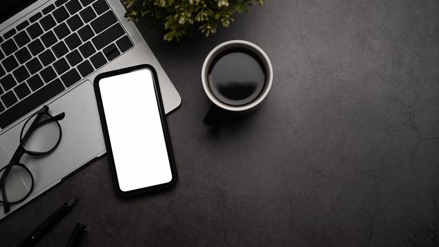 Contemporary workplace with mobile phone, laptop computer and coffee cup on dark stone background.
