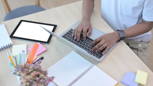 Cropped shot male office worker using laptop computer on wooden table.