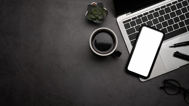 Top view, Flat lay. Smart phone, laptop computer, coffee cup and glasses on dark stone background.