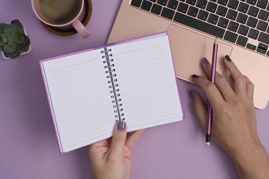 Woman hand holding notebook and using laptop computer on purple background.