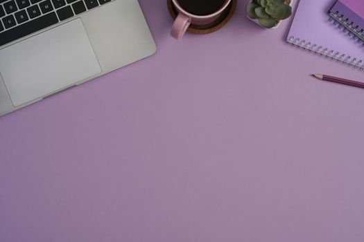 Top view computer laptop, notebook, succulent plants and coffee cup on purple background with copy space.