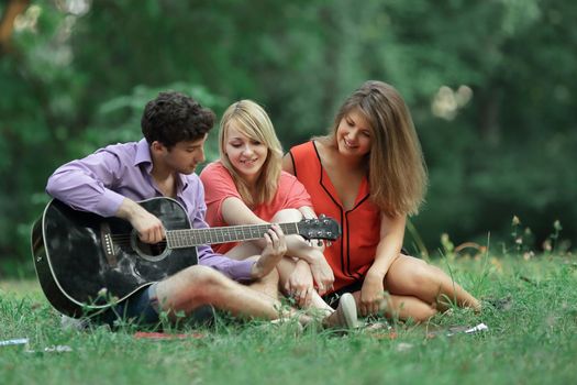 group of students with a guitar relax sitting on the grass in the city Park.