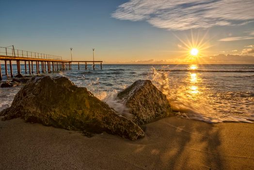 Sunrise over the sea with wave splashing on the rocks.