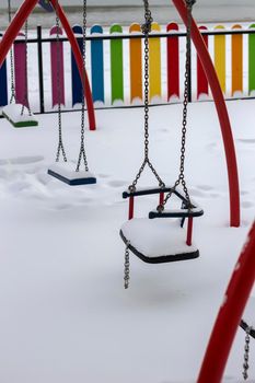 Snow on the playground. Winter composition with snow-covered swings.