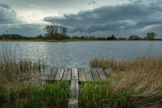 A pier in the reeds and a cloudy sky over the lake, spring day