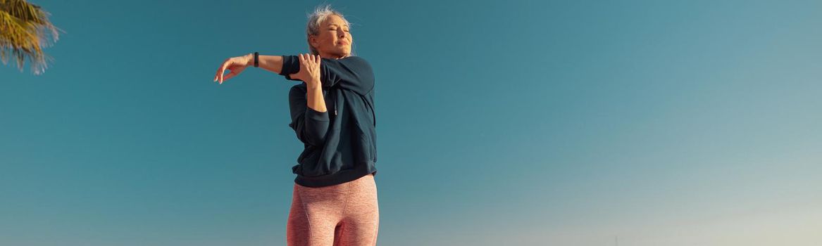 Motivated female in sportswear doing arm workout on the sports ground on a sunny day by the waterfront