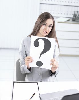 upset business woman holding a question mark ,sitting behind a Desk .photo with copy space.