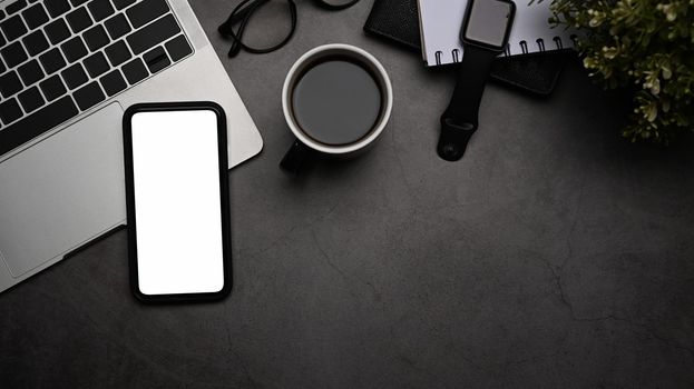 Smart phone with white screen, laptop computer, smart watch, coffee cup and eyeglasses on black table. Flat lay.