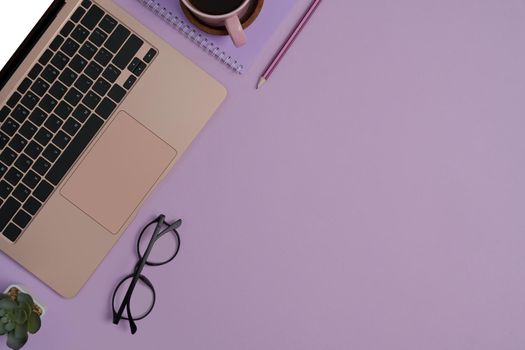 Laptop computer, eyeglasses, notebook, succulent plant and coffee cup on purple background with copy space.