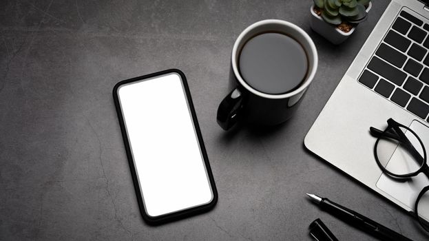 Top view modern workplace with mobile phone, laptop computer and coffee cup on dark stone background.