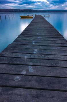 Tracks of steps on wooden pier and fishing boat at the lake after sunset