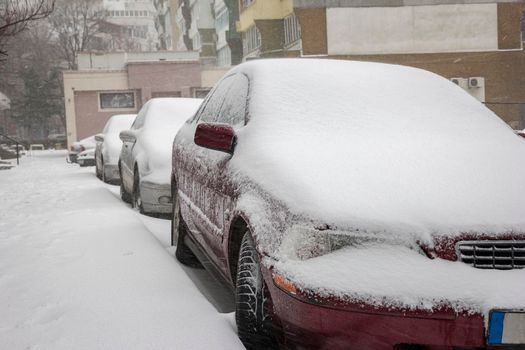 cars covered with snow on the street of the city in winter day