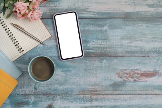Above view smart phone with white screen, notebook and coffee cup on wooden background. Copy space.
