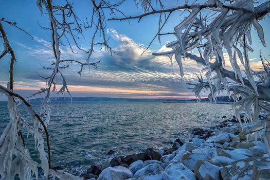 Sunrise/ sunset between icicles on tree branches frozen. Winter landscape 