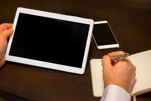Work place - a businessman writes information from a tablet to the notebook