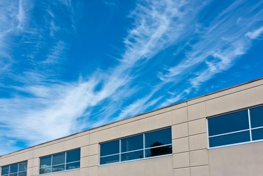Top of the office building with windows on blue and cloudy sky background.