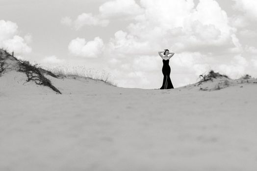 girl in a black long dress in a sandy desert under a blue sky