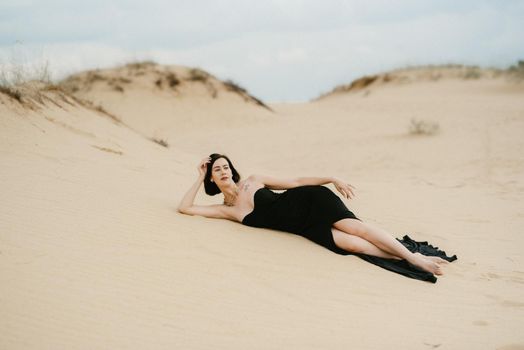 girl in a black long dress in a sandy desert under a blue sky