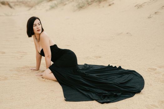 girl in a black long dress in a sandy desert under a blue sky