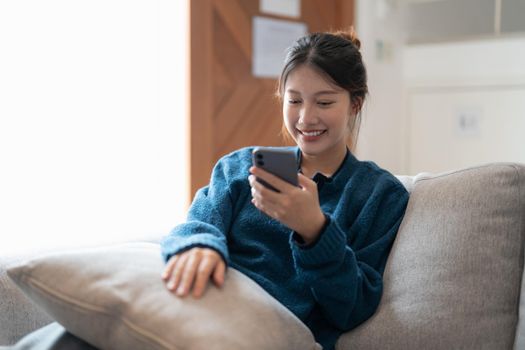 Happy casual beautiful asian woman is talking on a phone sitting on a sofa at home