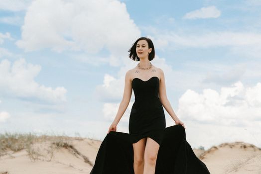 girl in a black long dress in a sandy desert under a blue sky