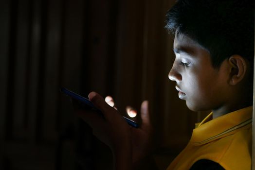 teenage boy sitting on sofa using smart phone at night .