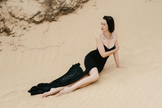 girl in a black long dress in a sandy desert under a blue sky