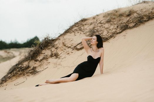 girl in a black long dress in a sandy desert under a blue sky