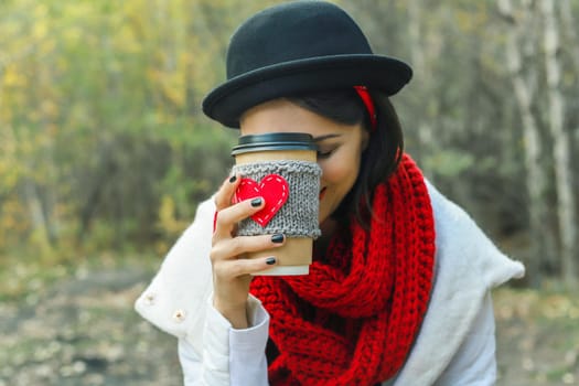 Young woman in a black hat drinks coffee from cozy cup on the nature. Bright smile and good mood