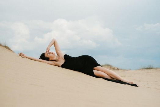 girl in a black long dress in a sandy desert under a blue sky